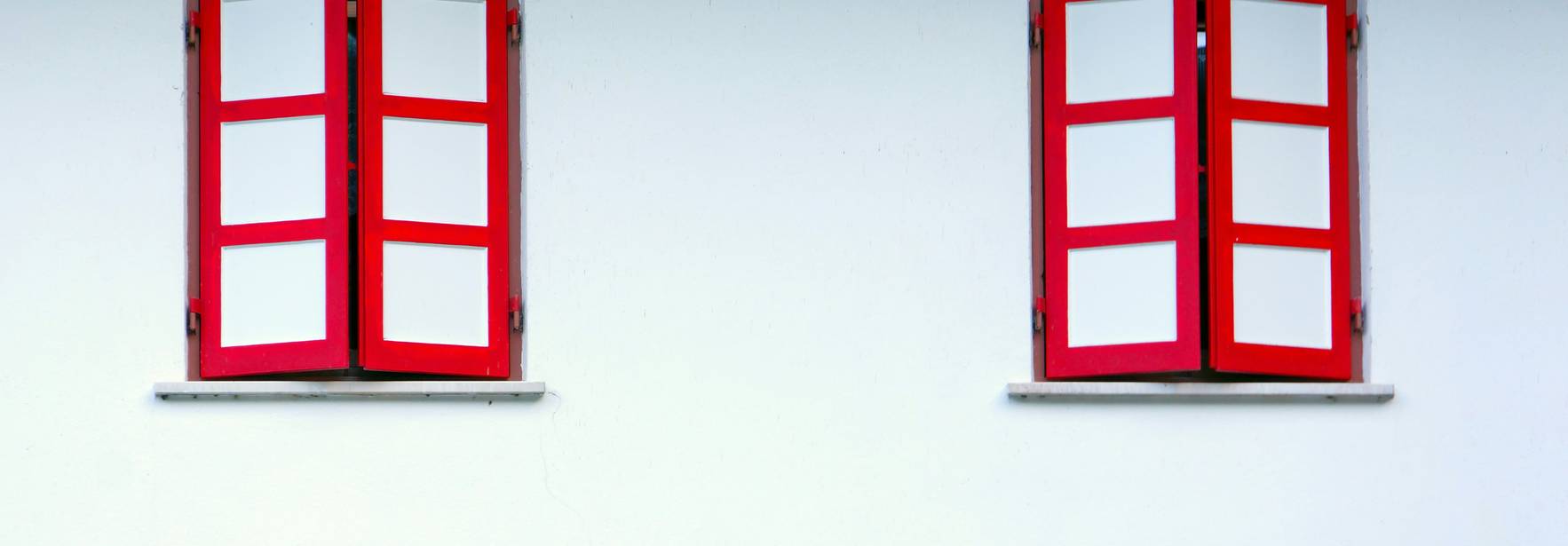 Dos ventanas con marcos rojos en una pared blanca.