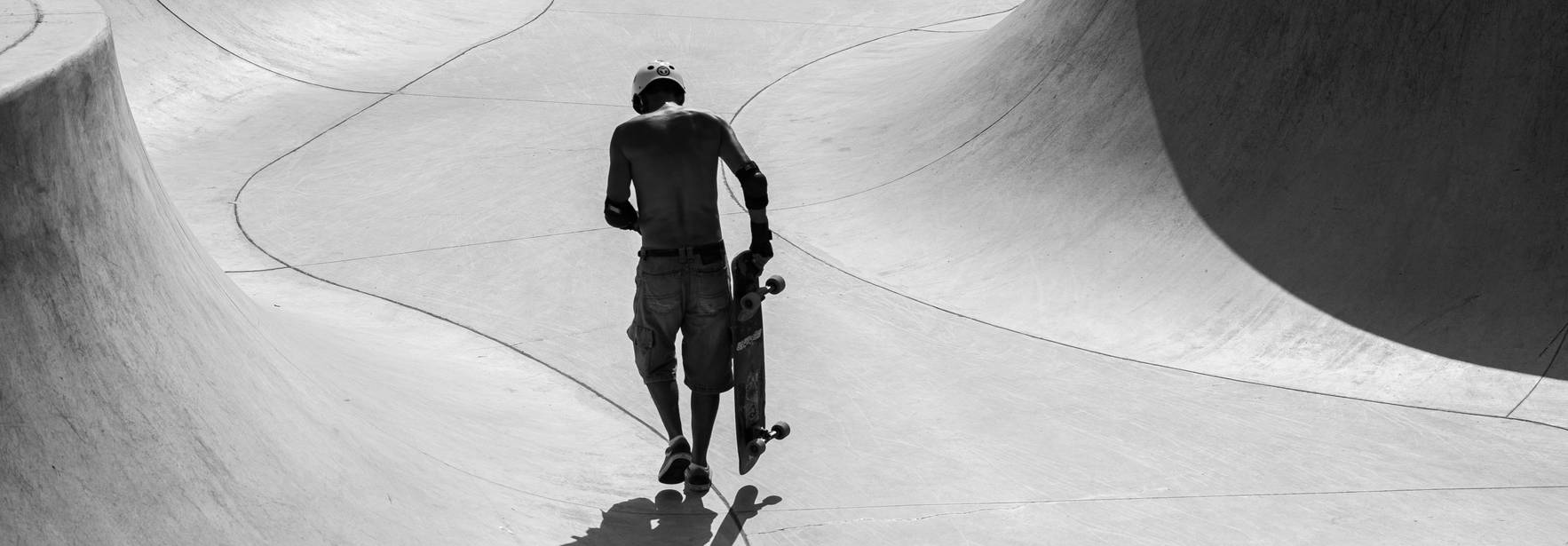 Un skater camina por un parque de patinaje vacío y curvado.