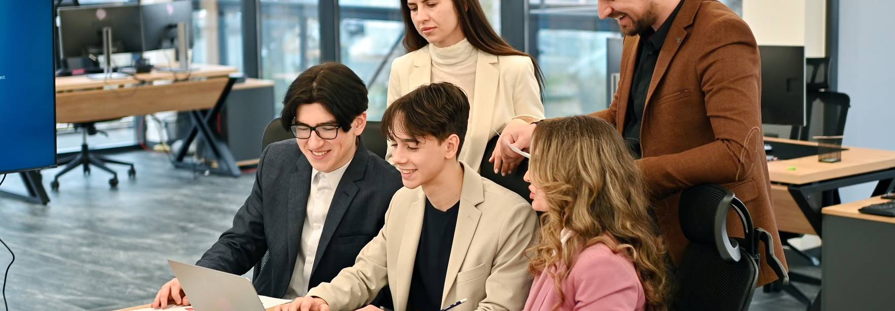 Un grupo de cinco personas está trabajando y colaborando en una oficina moderna frente a una computadora portátil.