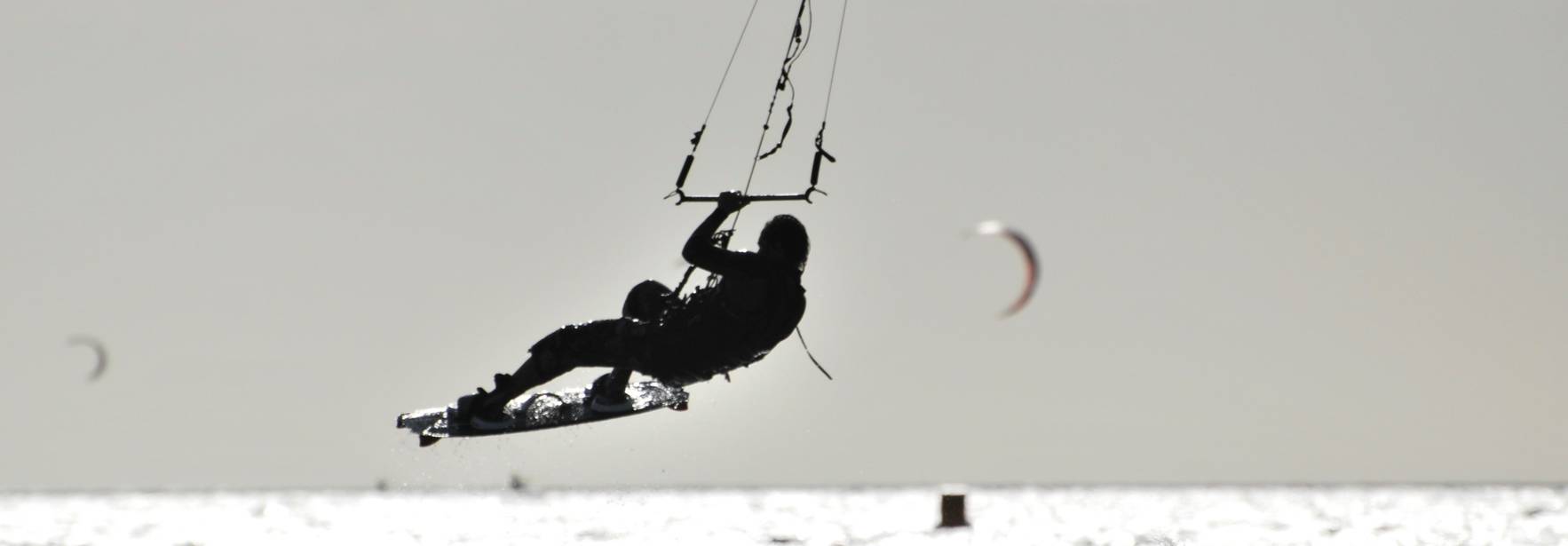 Una persona practicando kitesurf en el mar con varias cometas al fondo.