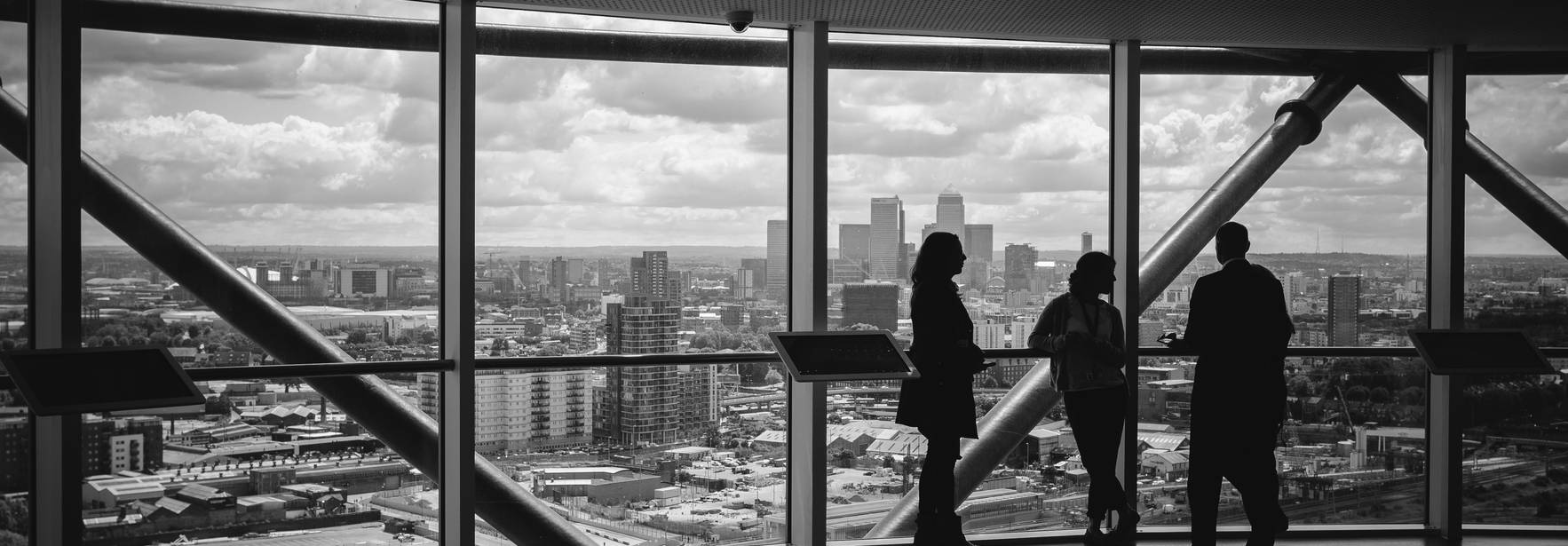 Un grupo de personas observa la ciudad desde una gran ventana en un ambiente urbano.