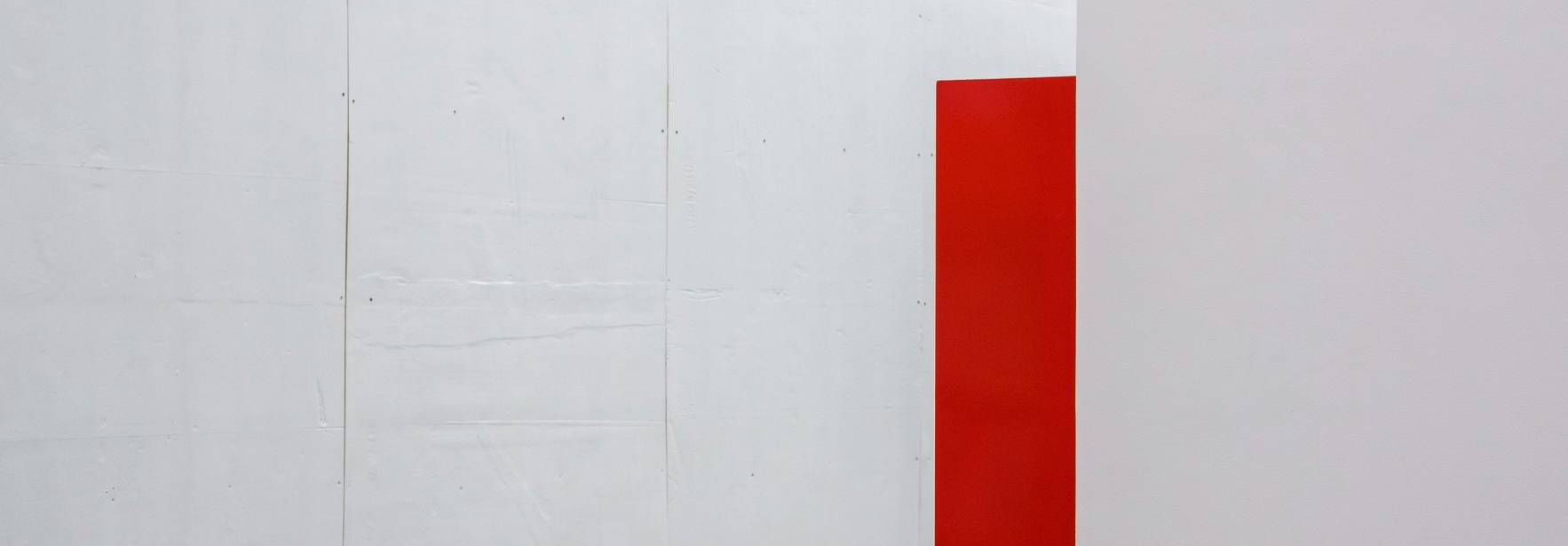 La imagen muestra una pared blanca con un panel rojo en un lado.