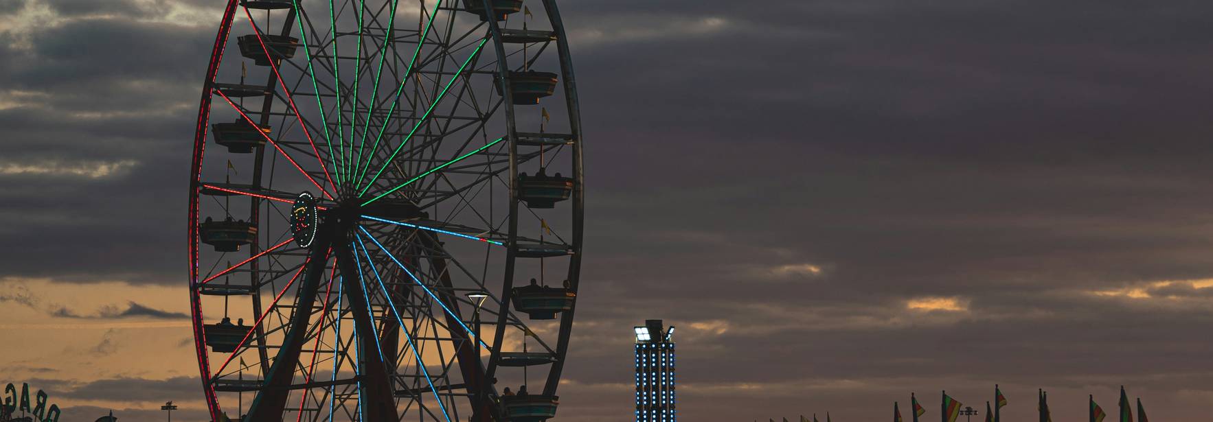 La imagen muestra una noria iluminada en un parque de diversiones durante el atardecer.