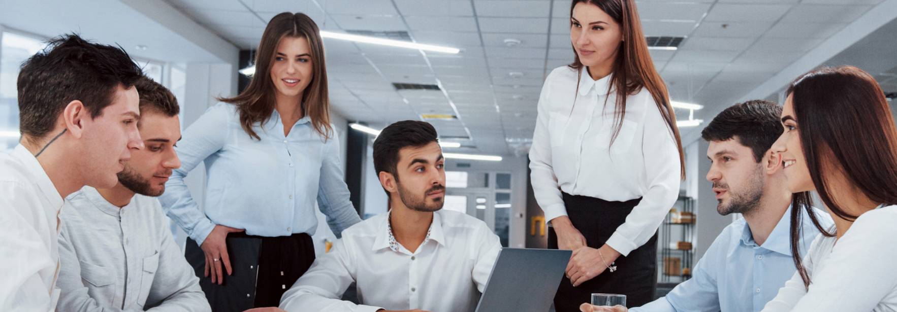 Un grupo de seis personas en una reunión colaborativa alrededor de una mesa con una computadora portátil.