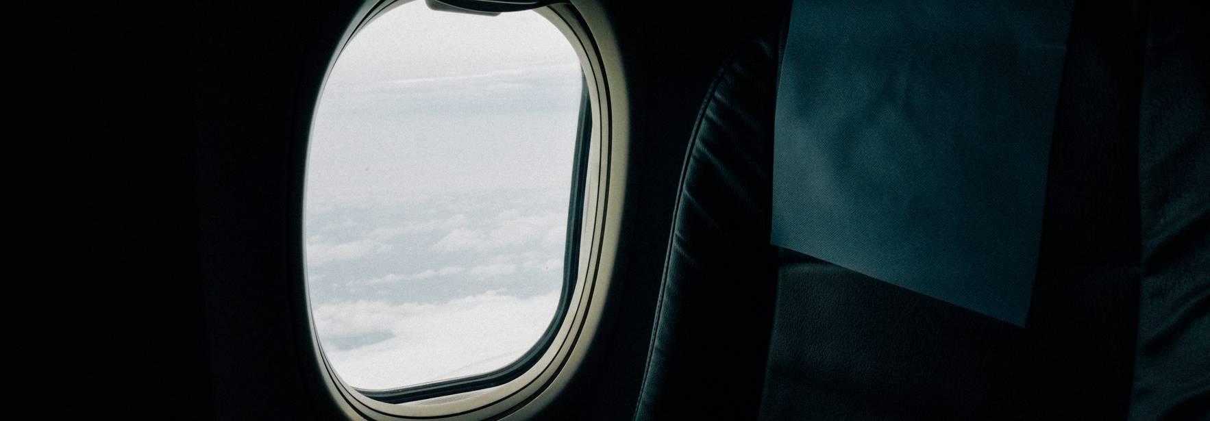 Vista desde un asiento de avión mostrando una ventanilla con nubes afuera.