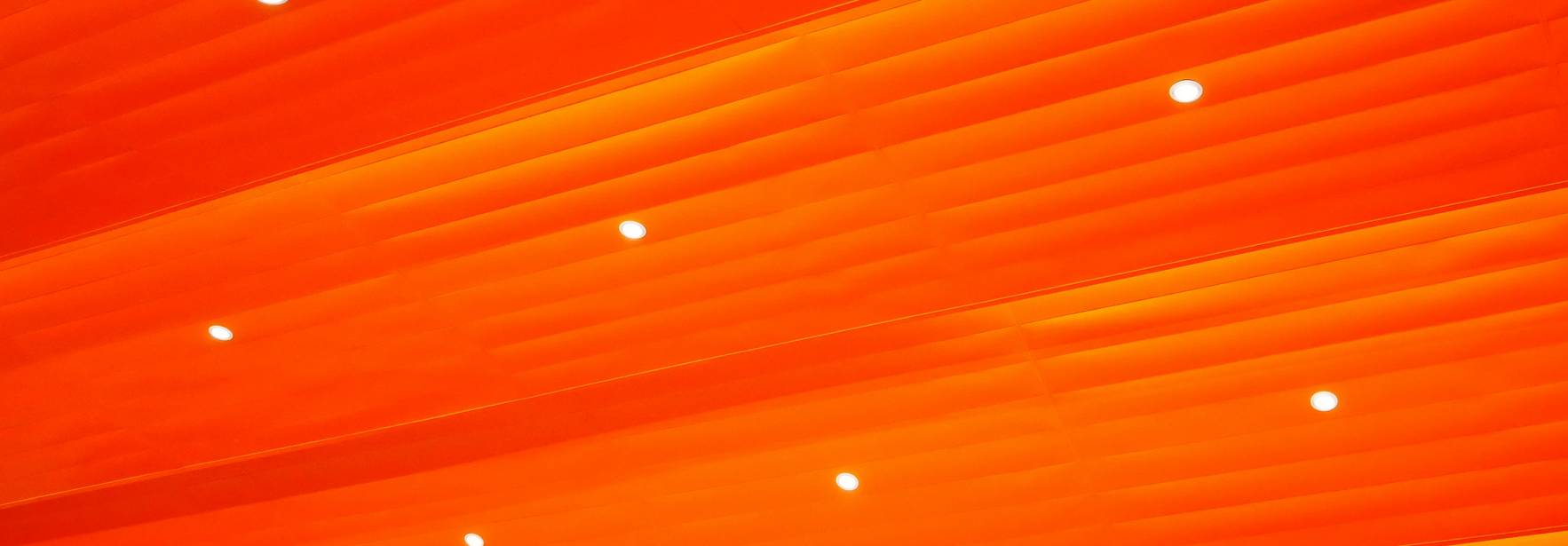 La imagen muestra un techo con paneles de color naranja y luces brillantes distribuidas uniformemente.