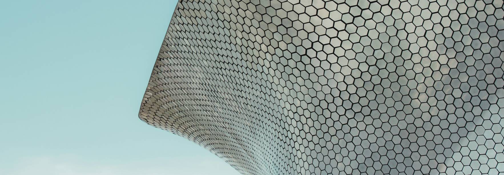 Una estructura arquitectónica con una fachada de paneles hexagonales contra un cielo azul claro.