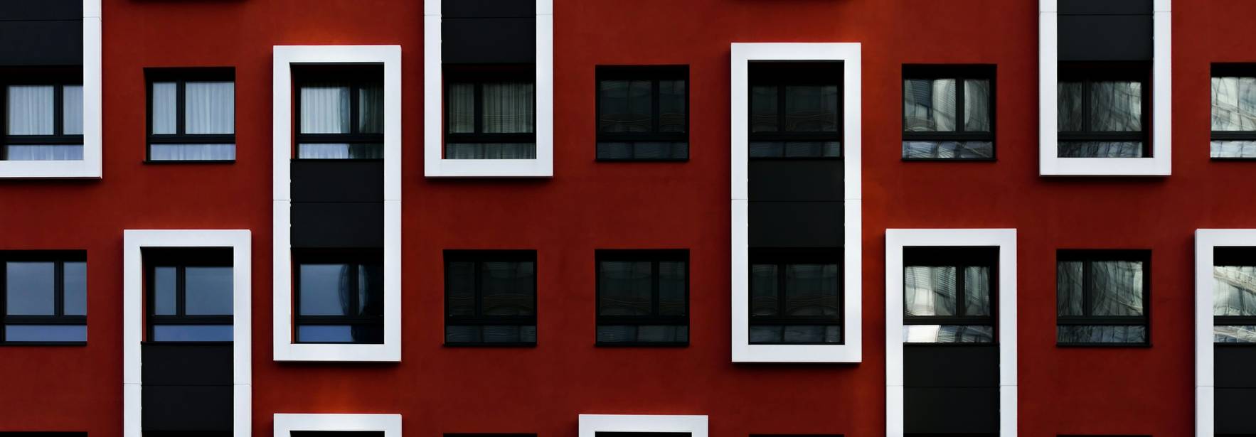 Una fachada moderna de un edificio con un diseño de ventanas asimétrico en tonos rojos y negros.