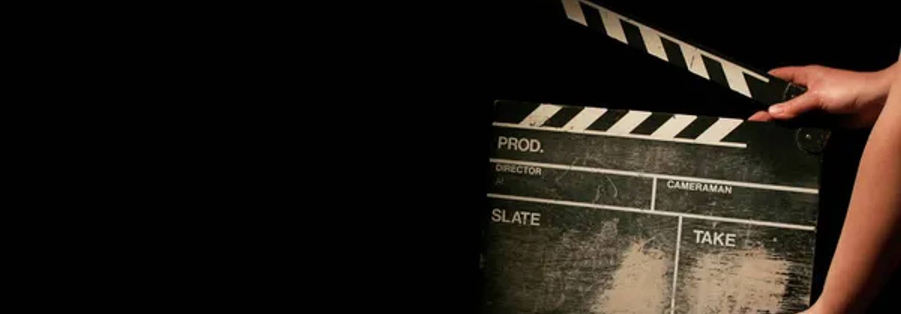 Una persona sostiene una claqueta de cine en un entorno oscuro.