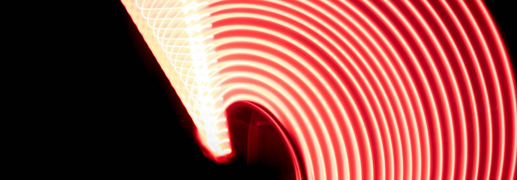 La imagen muestra un patrón de luces rojas en forma de espiral sobre un fondo negro.