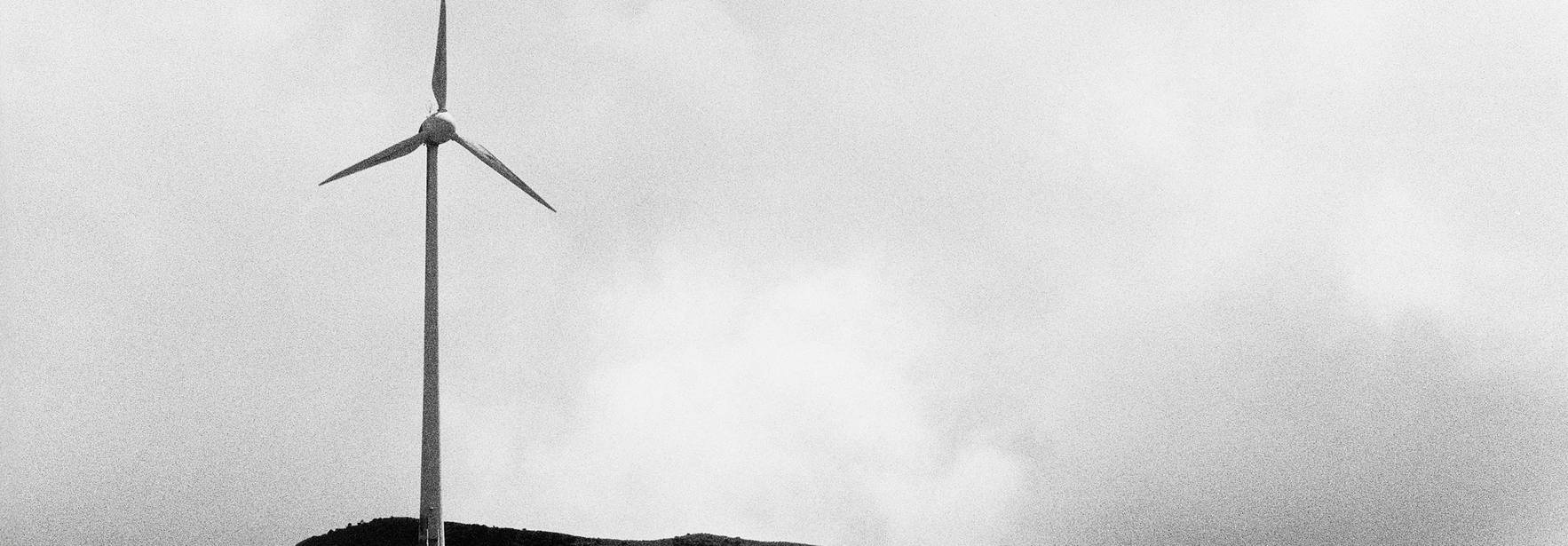 En la imagen se observa un molino de viento solitario en una colina con un fondo nublado.