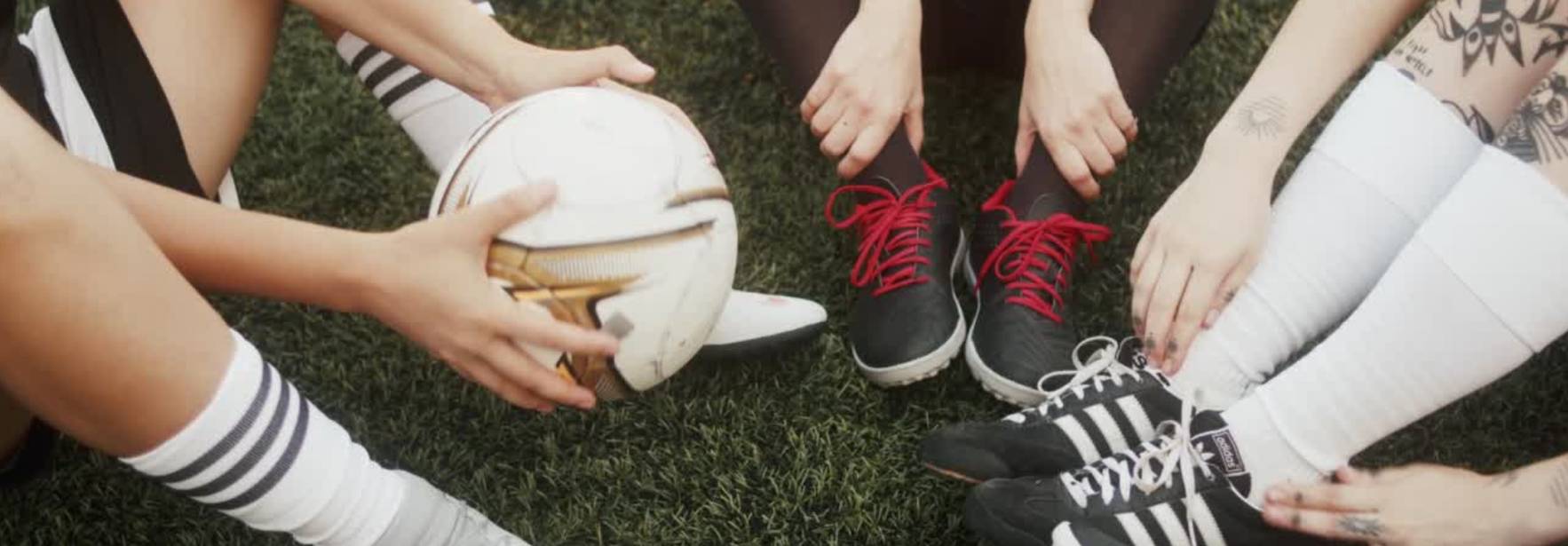 Un grupo de personas se reúne en el campo de fútbol, sosteniendo un balón y mostrando sus zapatos deportivos.