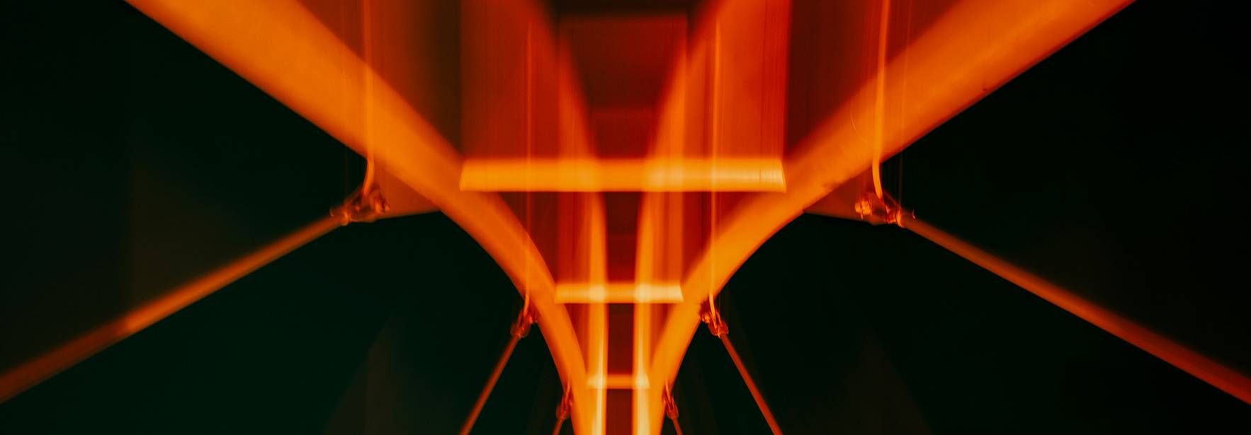 La imagen muestra un puente iluminado con luces de tono naranja contra un fondo oscuro.