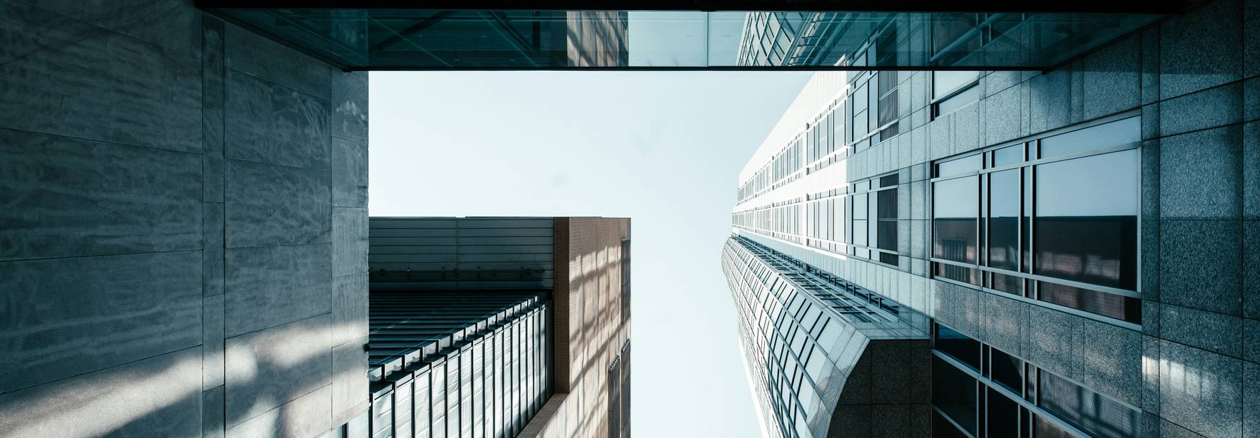 Una vista arquitectónica hacia arriba entre edificios altos que muestran reflejos de luz sobre superficies brillantes.