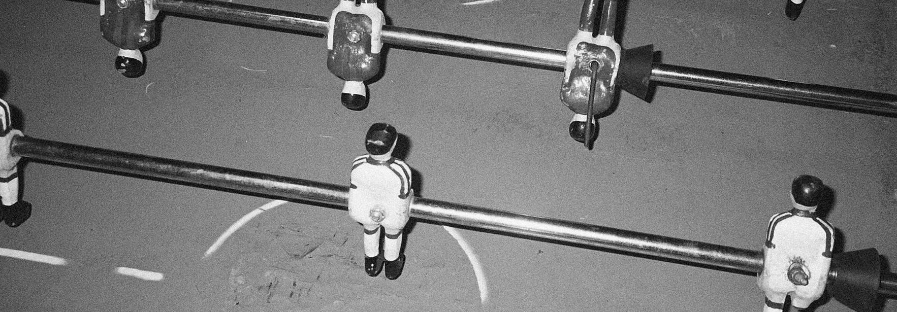 Una vista cenital de una mesa de futbolín con figuras de jugadores dispuestas en alineación.