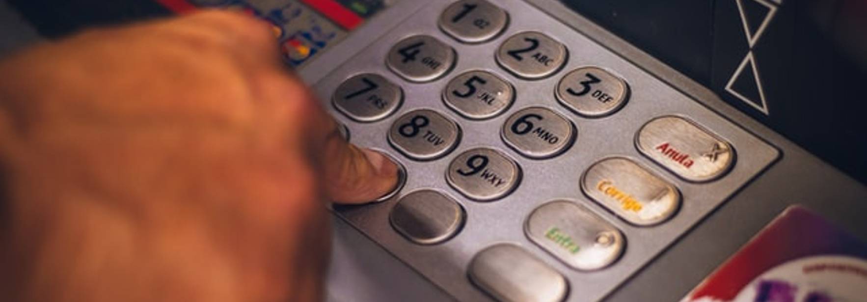 Una persona está utilizando un teclado numérico de un cajero automático con una tarjeta bancaria a un lado.