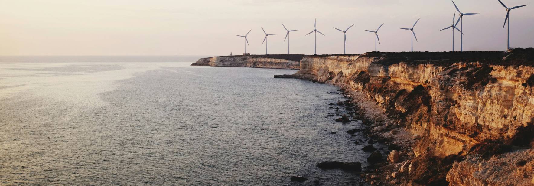 Una vista del mar y acantilados con aerogeneradores en el horizonte durante el atardecer.