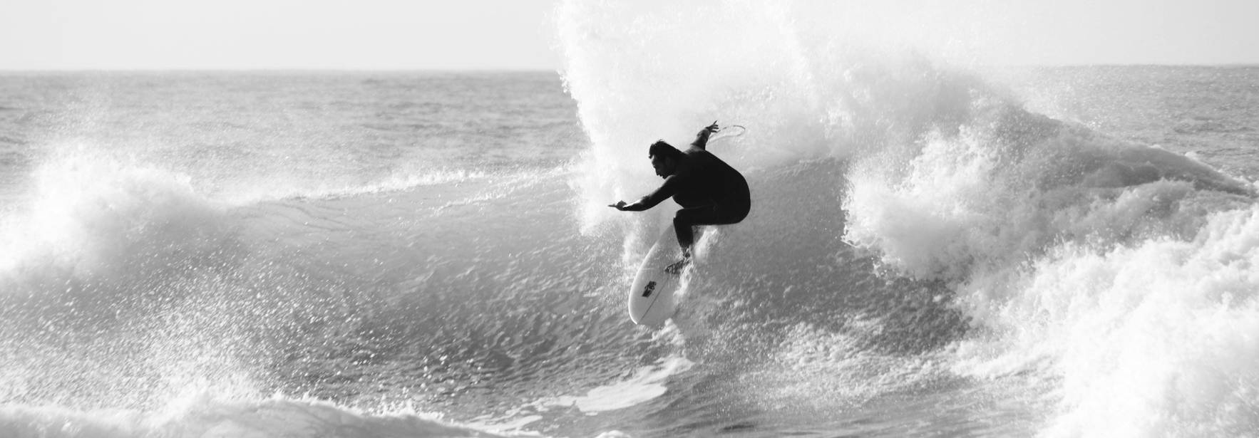 Un surfista ejecutando una maniobra sobre una ola en blanco y negro.