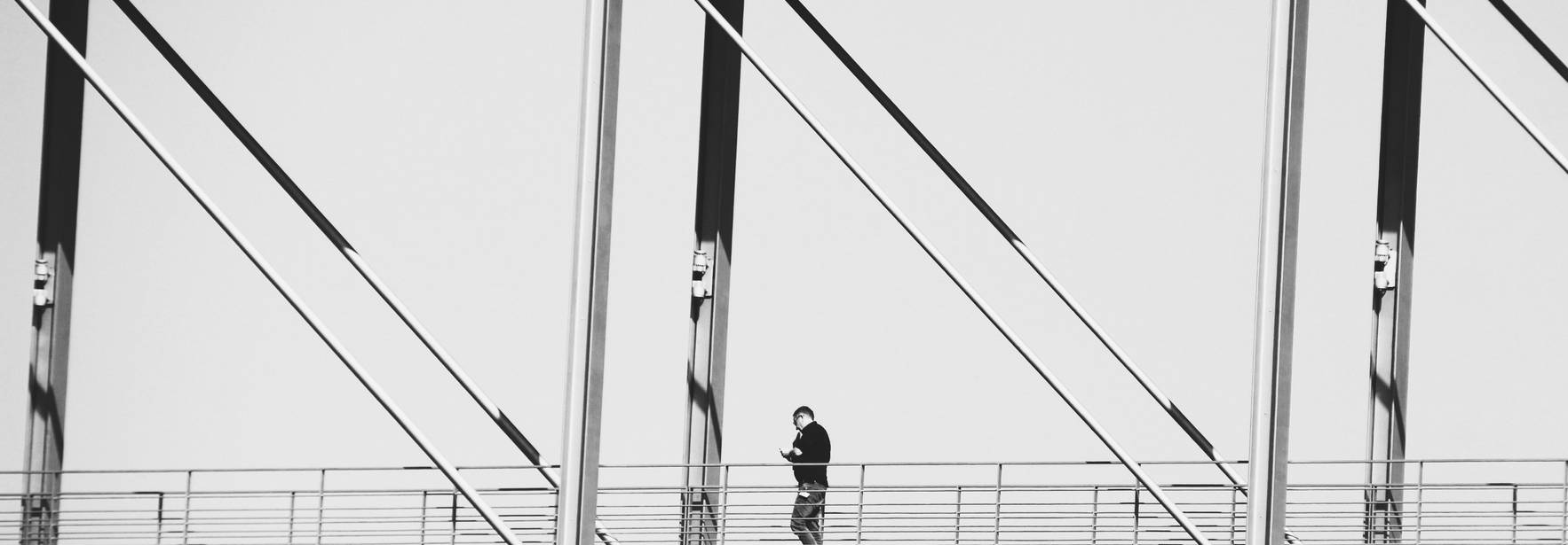 Una persona camina sola sobre un puente moderno en blanco y negro.