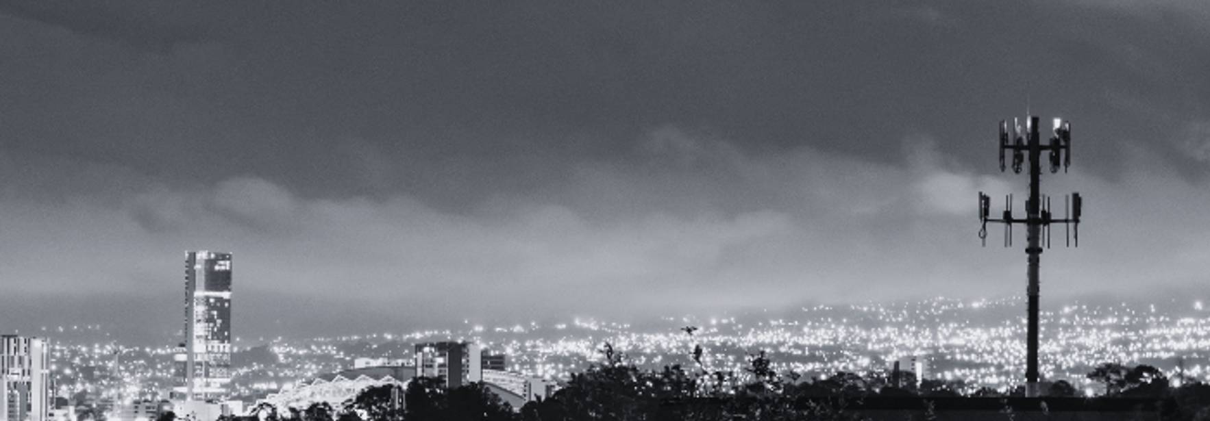 Una vista nocturna de una ciudad iluminada con torres y nubes en el horizonte.