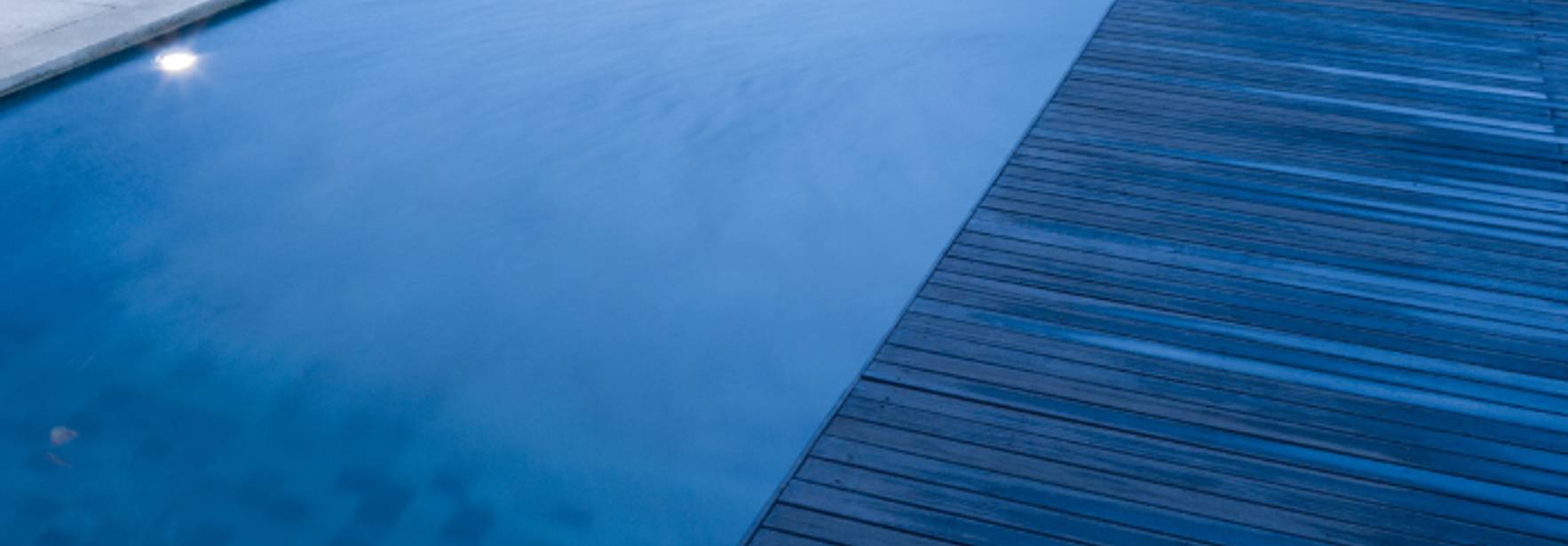 Una vista de un área de piscina con un muelle de madera y luces reflejándose en el agua.