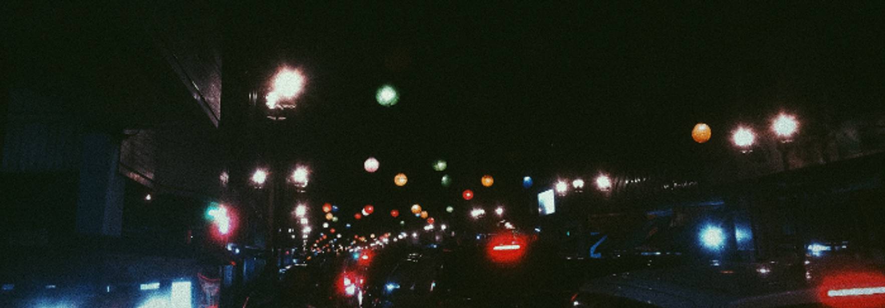 Una calle iluminada por faroles en una noche oscura con coches detenidos.