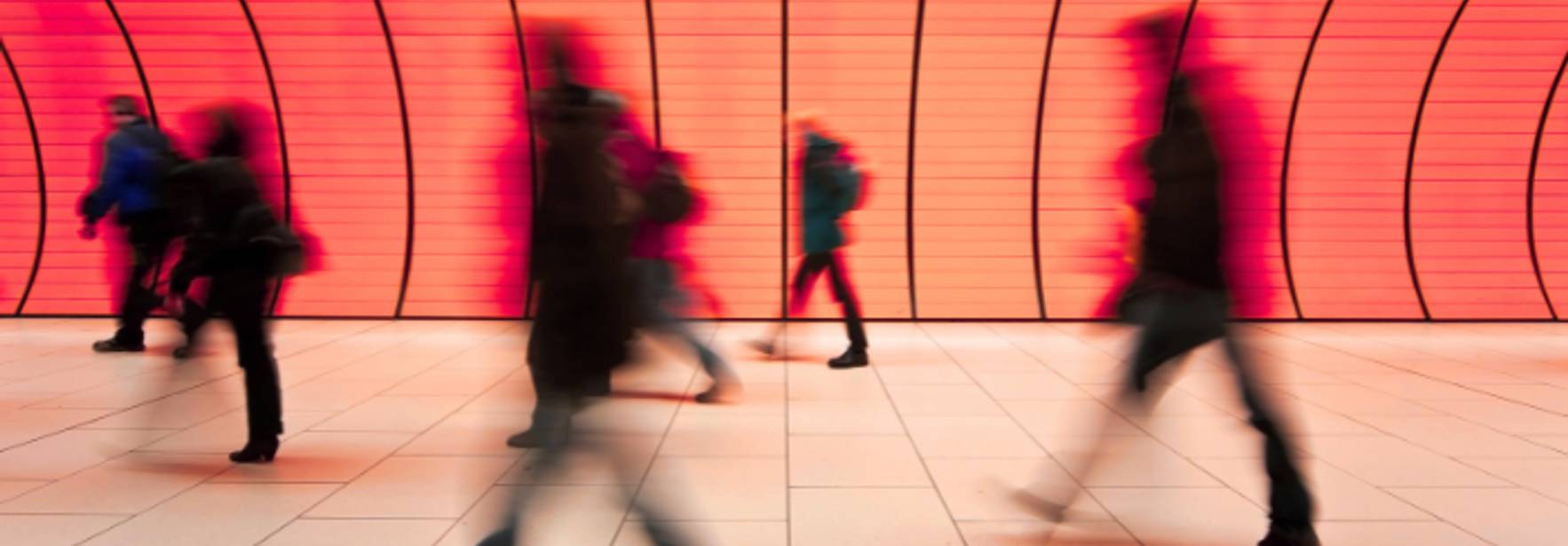 Un grupo de personas camina rápidamente frente a una pared iluminada en tonos rojos.