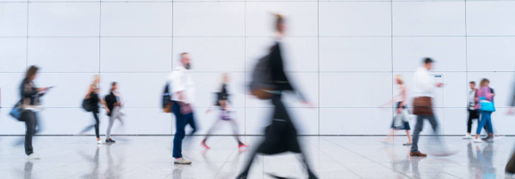 Una multitud de personas caminando rápidamente en un espacio moderno y luminoso de un aeropuerto.