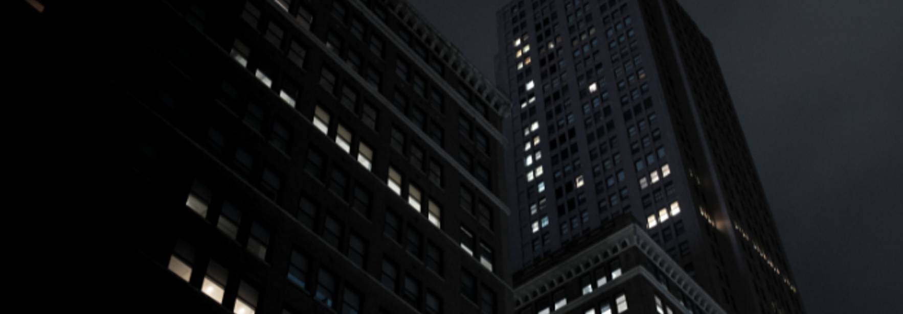 Una escena urbana nocturna con edificios iluminados sutilmente bajo un cielo oscuro.