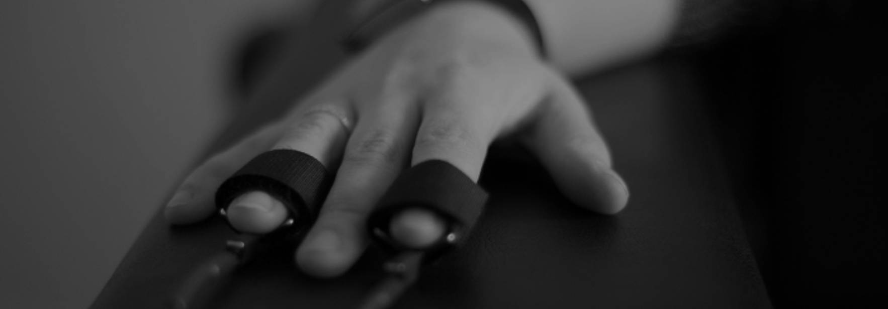 Una mano con anillos en los dedos descansa sobre una superficie oscura.