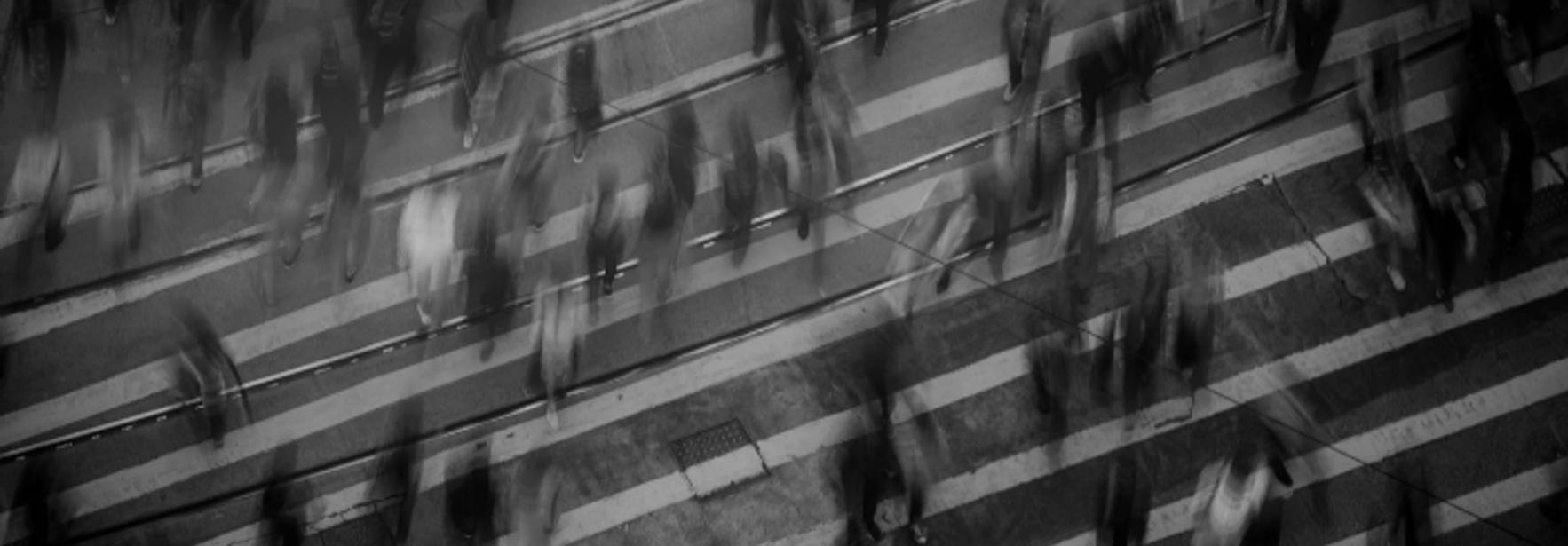 Una multitud de personas camina de forma difusa sobre unas franjas peatonales en un ambiente urbano.