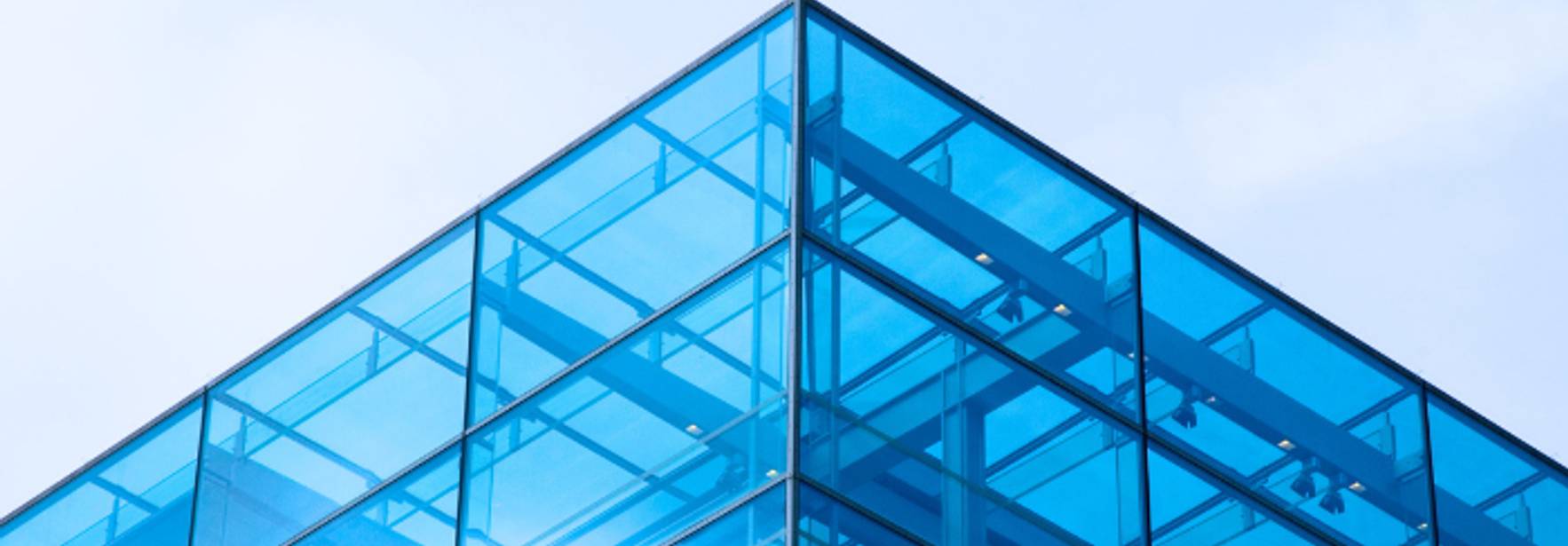 La imagen muestra la esquina superior de un edificio moderno con una fachada de cristal azul.