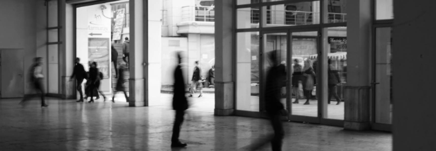 Una imagen en blanco y negro que muestra un espacio interior con personas caminando hacia la salida.