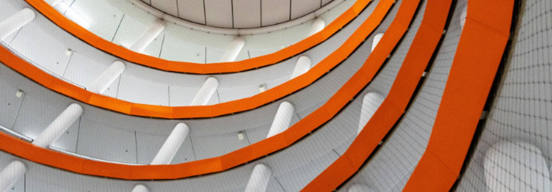 Una vista desde abajo de una estructura arquitectónica en forma de espiral con colores naranja y blanco.