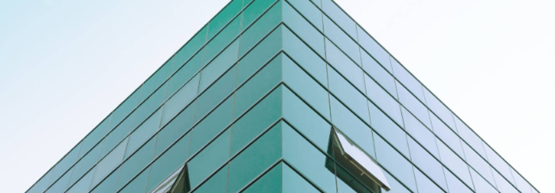 La imagen muestra la esquina de un edificio moderno con fachadas de vidrio reflejante.
