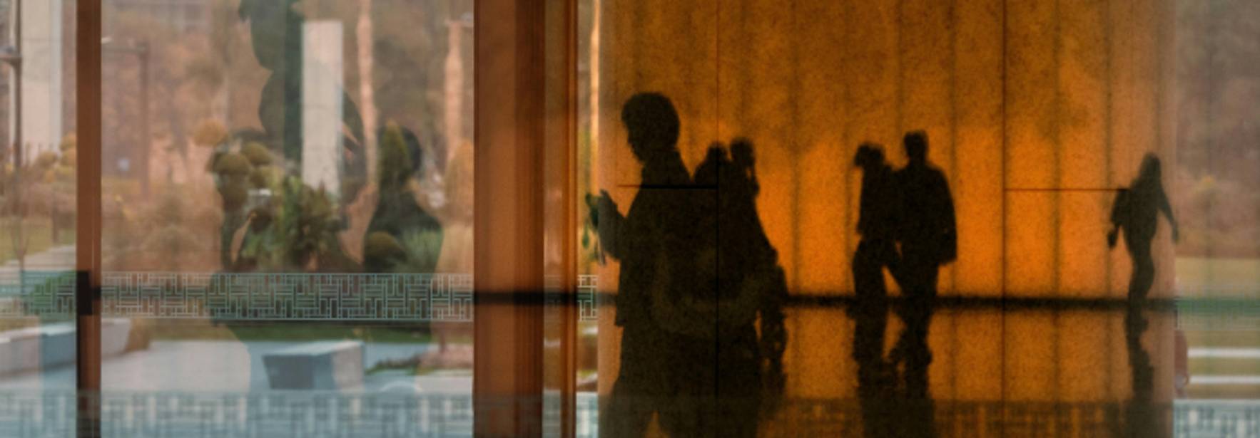 La imagen muestra siluetas de personas reflejadas en una superficie brillante con un fondo de colores cálidos.