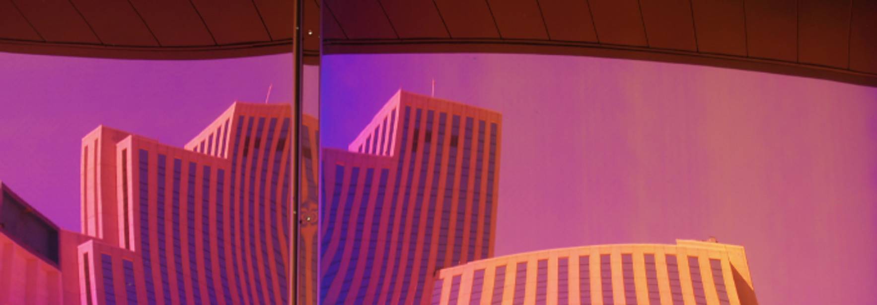 La imagen muestra el reflejo de edificios en una superficie brillante con tonos púrpuras y naranjas.