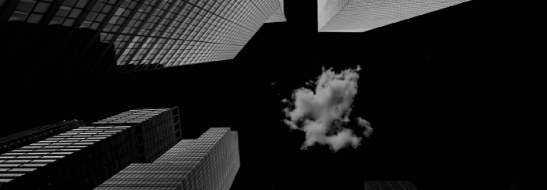 La imagen muestra un ángulo bajo de altos edificios rodeando un cielo oscuro con una nube blanca.