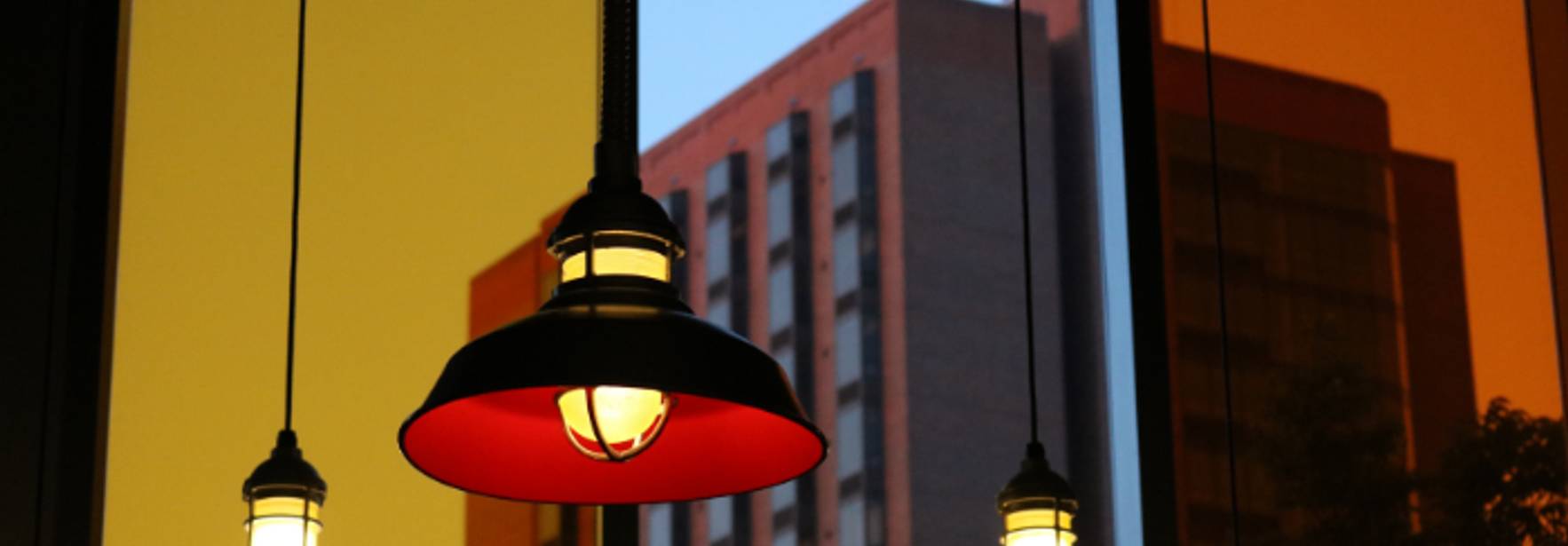 Una imagen que muestra lámparas colgantes en un entorno urbano iluminado por una puesta de sol.