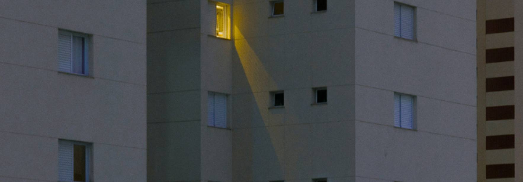 Una luz amarilla se emite desde una ventana de un edificio gris durante la noche.