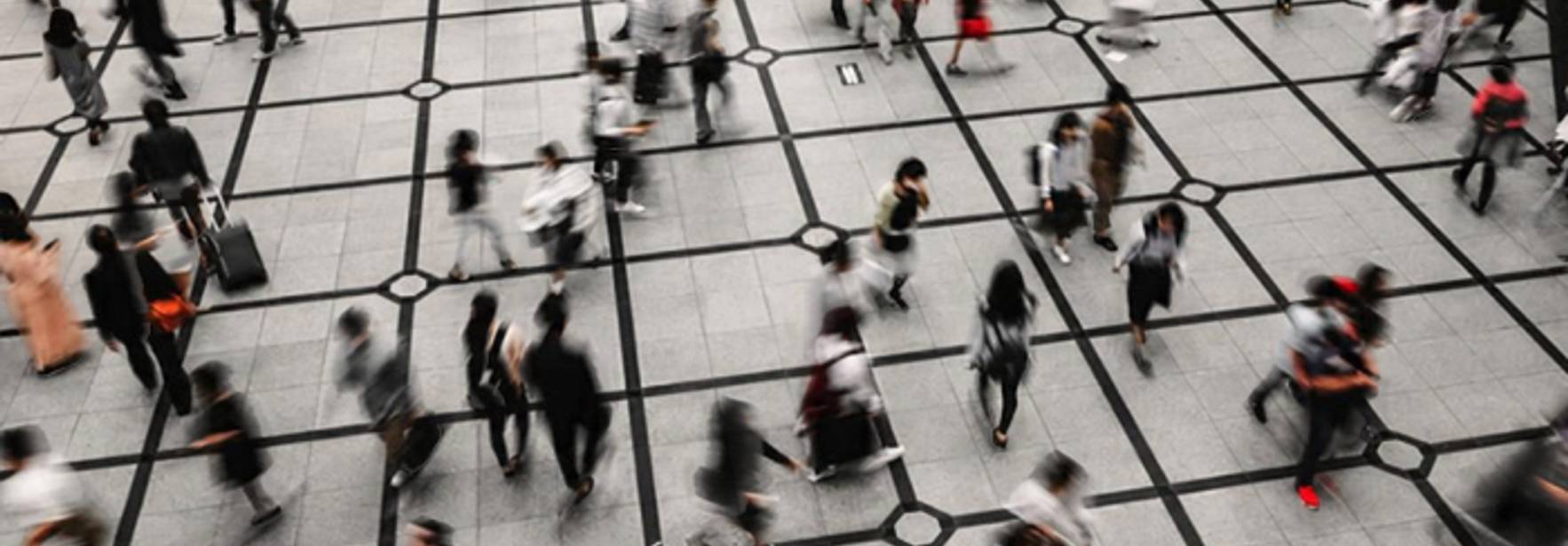 Una multitud de personas se mueve rápidamente por un espacio urbano con un diseño de piso cuadriculado.