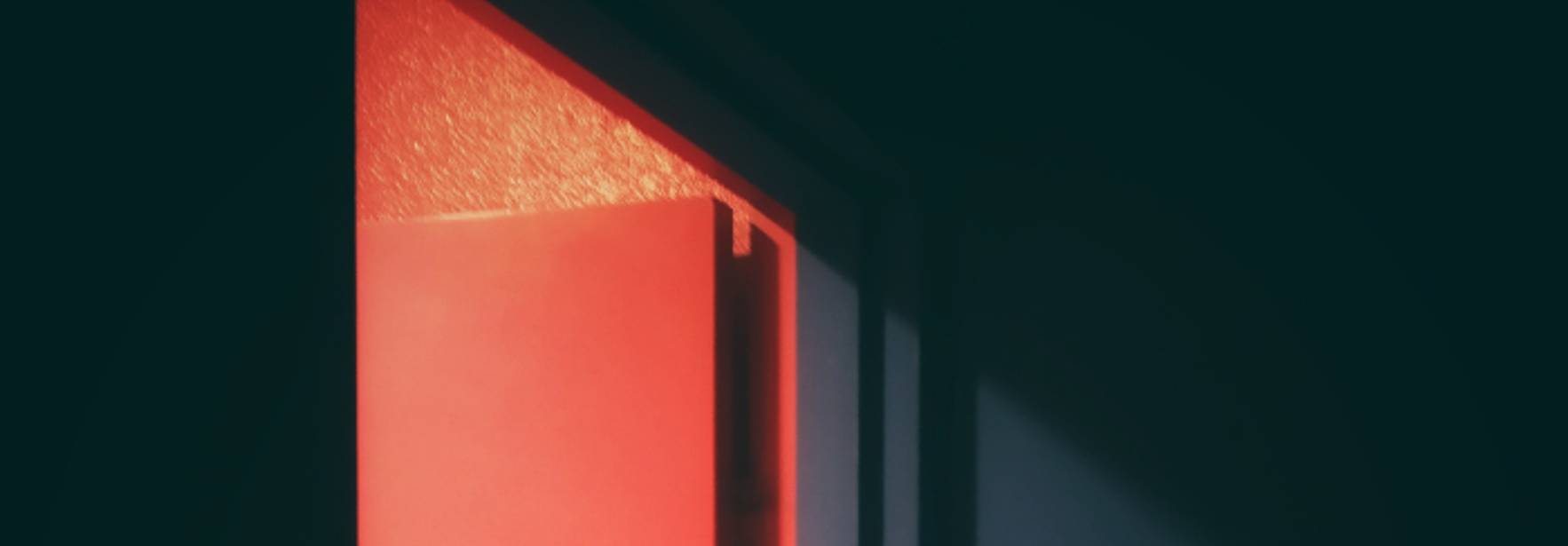 Una puerta entreabierta emite una luz roja en un ambiente oscuro.