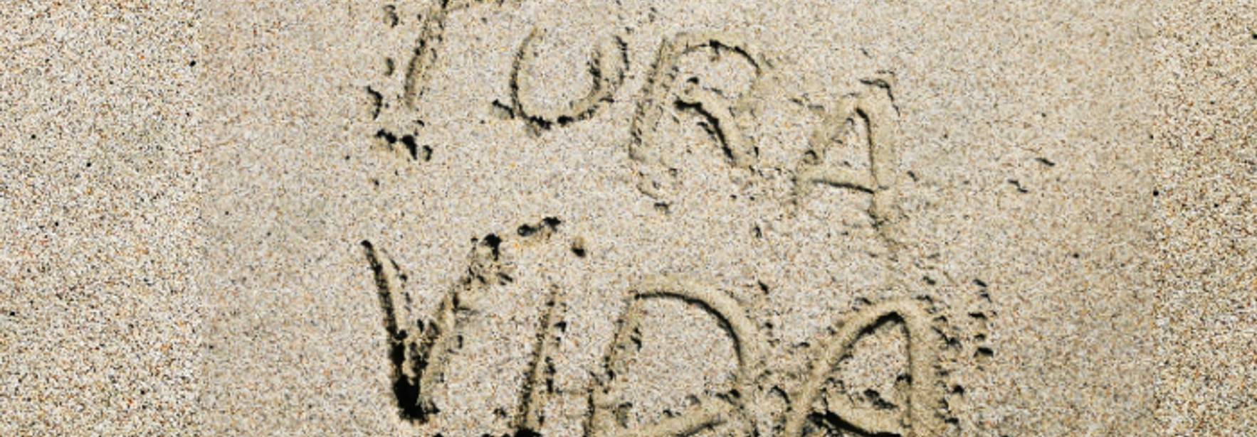 La imagen muestra la frase 'Pura Vida' escrita en la arena de una playa.