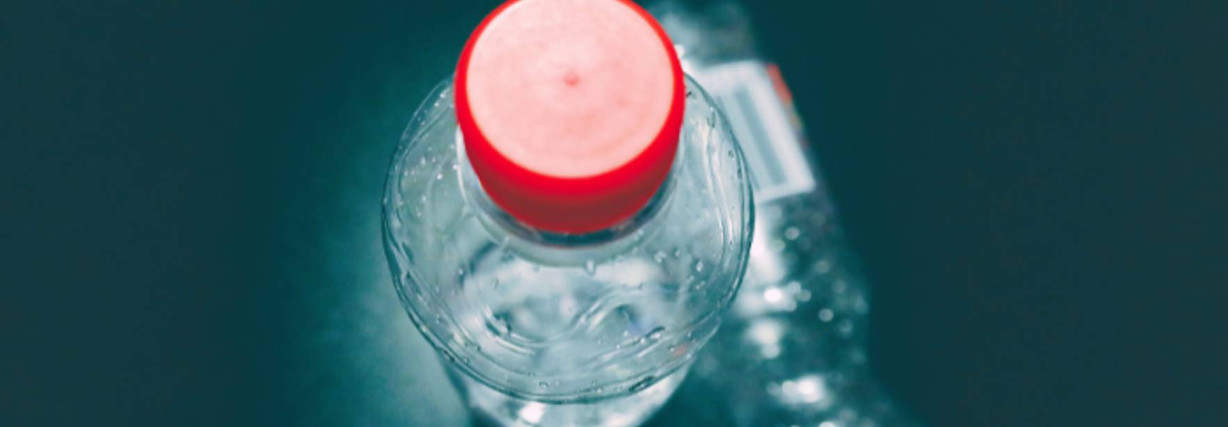 Una botella de agua con tapa roja en primer plano y otra botella en el fondo.