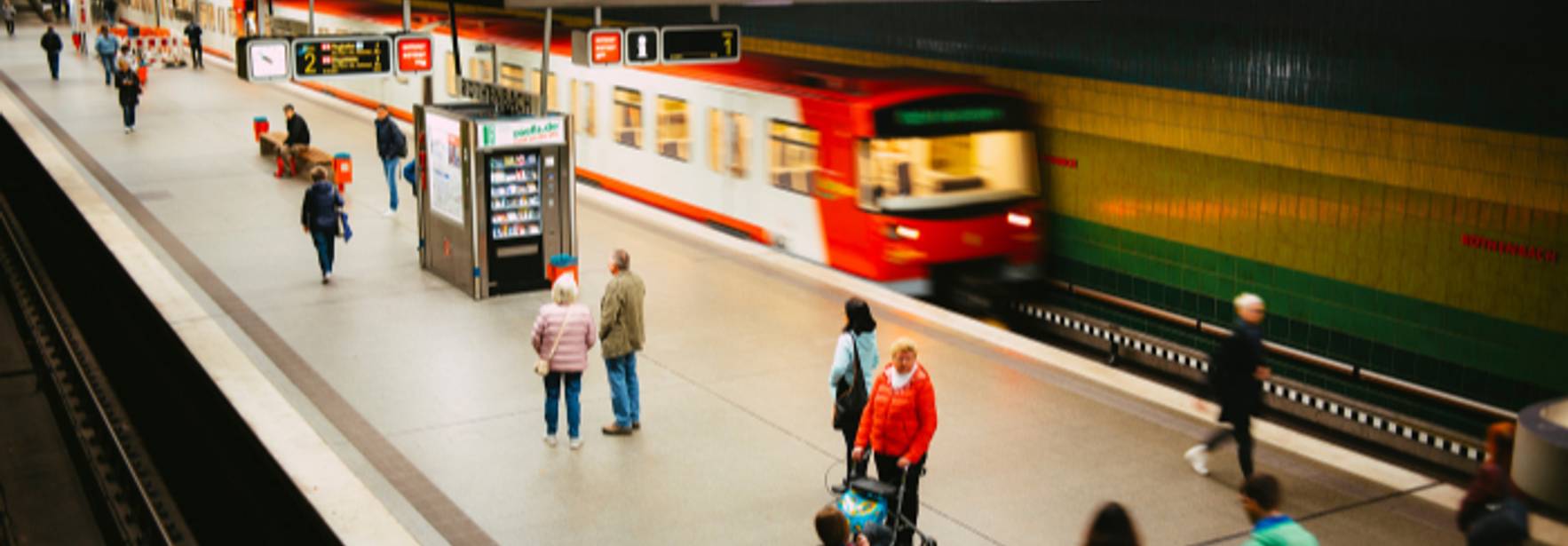 Una estación de tren con pasajeros esperando y un tren en movimiento.