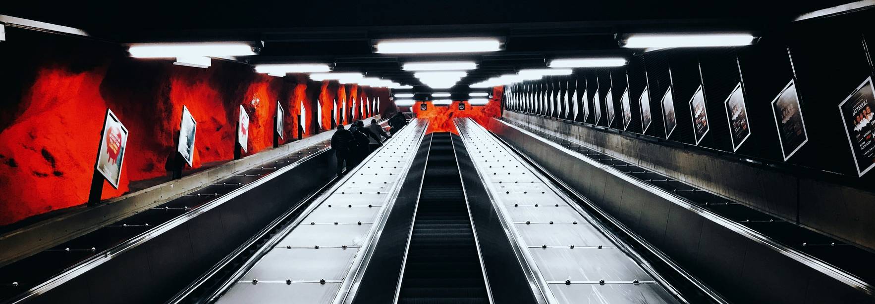 Una escalera mecánica en un entorno urbano con paredes rojas y luces brillantes.