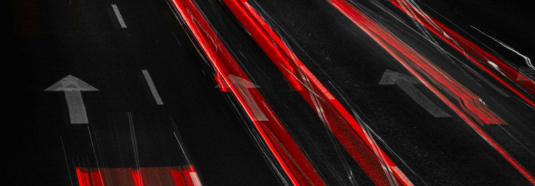 La imagen muestra el movimiento de vehículos en una carretera oscura, con luces rojas dejando estelas brillantes.