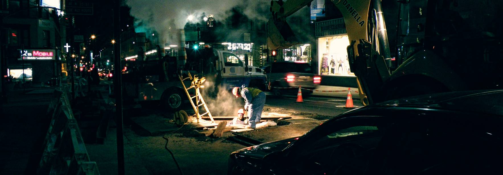 Una escena nocturna de trabajos de construcción en la calle con humo y maquinaria pesada.
