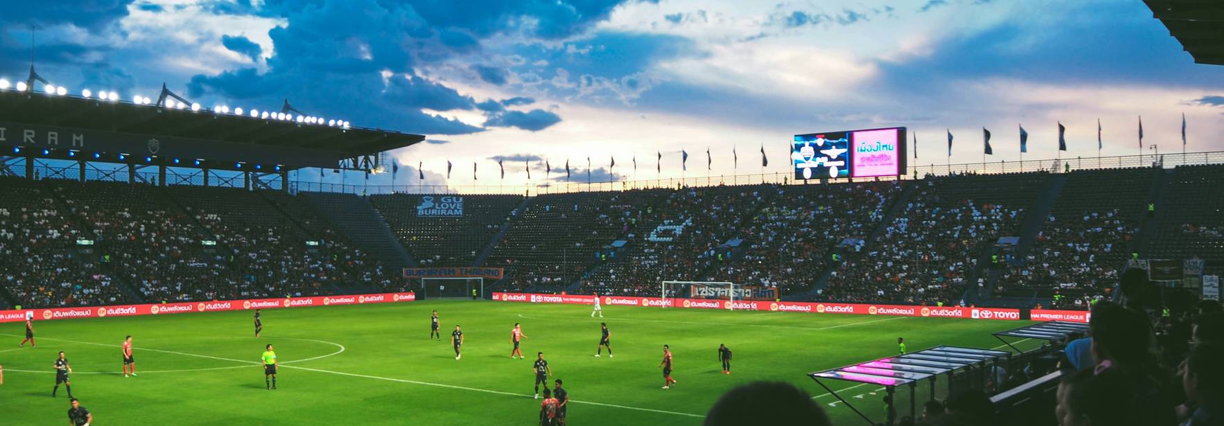 Un partido de fútbol con un cielo atardecido y una gran multitud de espectadores en las gradas.