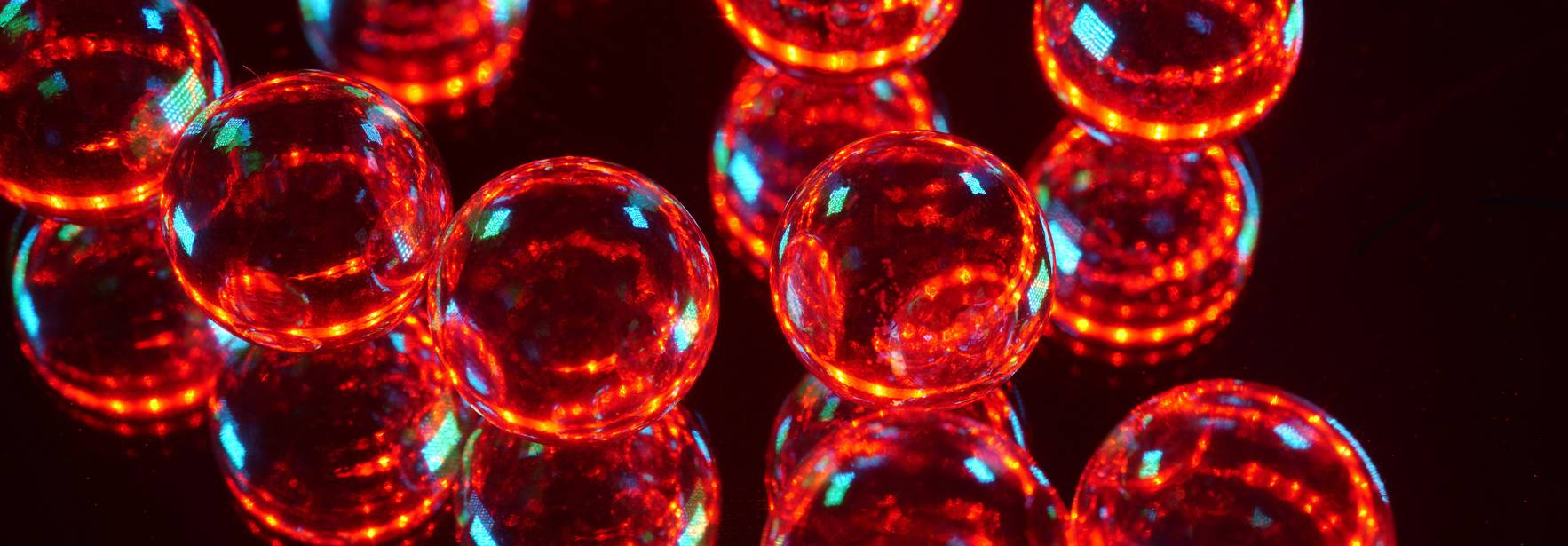 Esferas de vidrio rojas brillantes sobre una superficie reflejante.